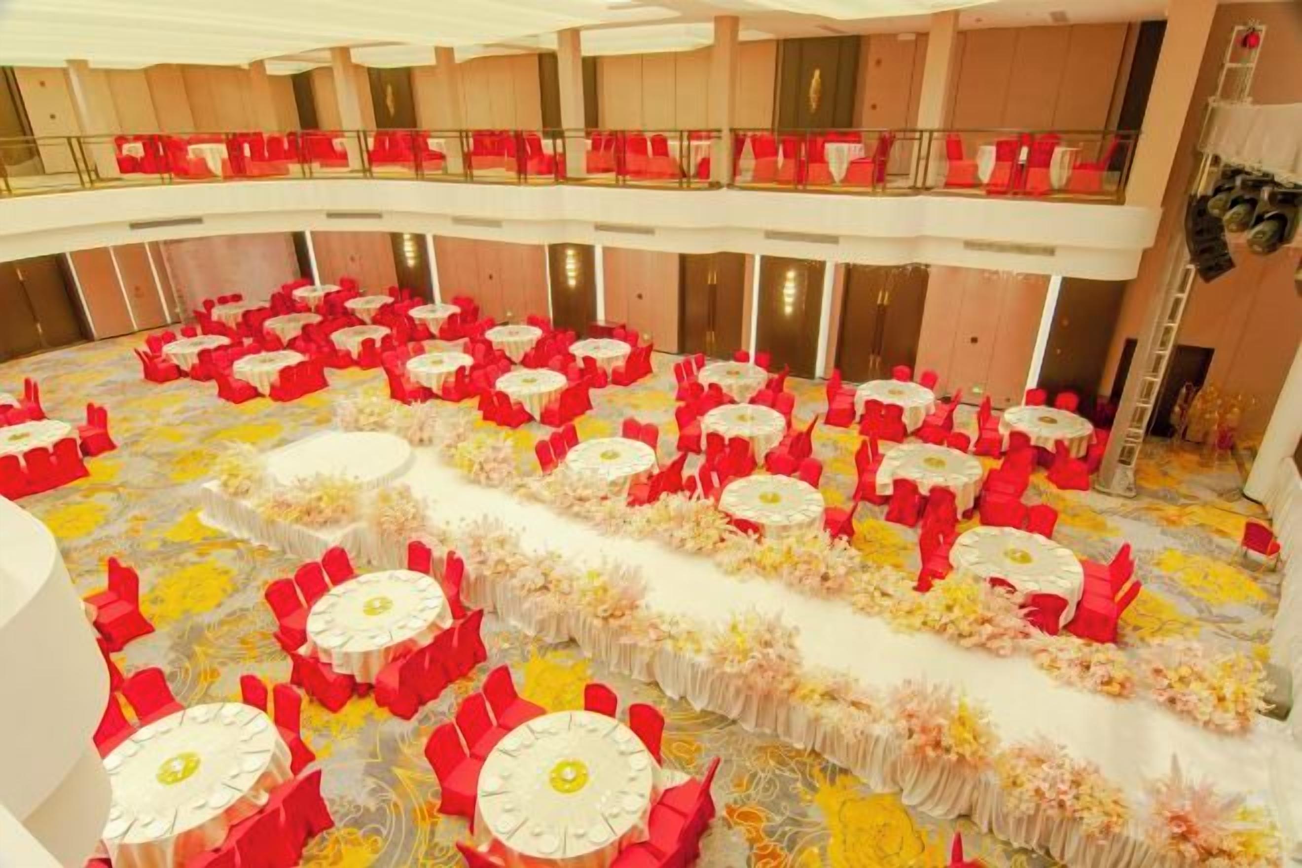 A large hall with multiple round tables arranged in rows, each with red chairs and white tablecloths.
