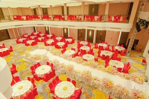 A large hall with multiple round tables arranged in rows, each with red chairs and white tablecloths.