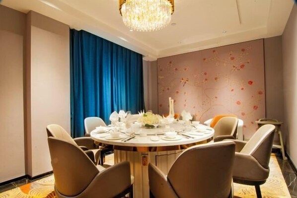 A dining area with a round table set for four, blue curtains, a chandelier, and a floral wall design. - Huayuan Hotel (Xiantao)