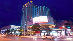A multi-story hotel with a prominent curved corner and illuminated signage. - Huayuan Hotel (Xiantao)