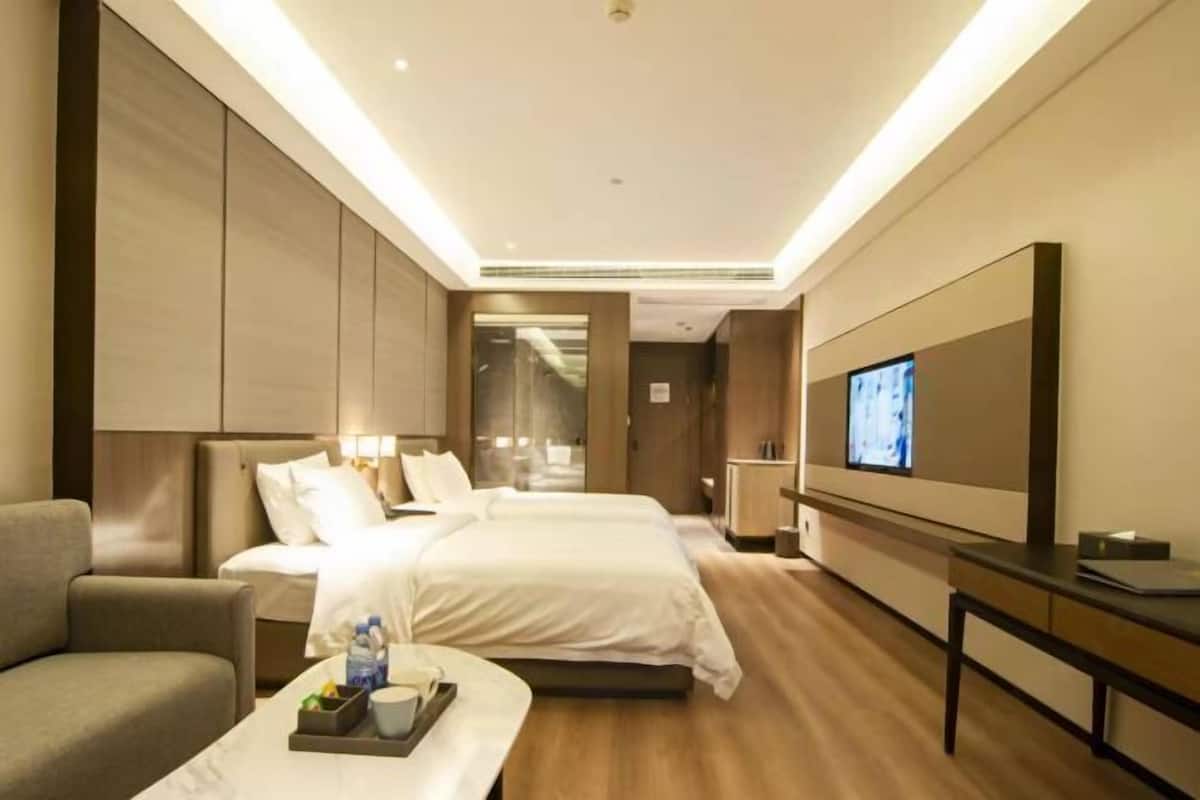 A hotel room with two beds, a TV, a desk, and a sofa.