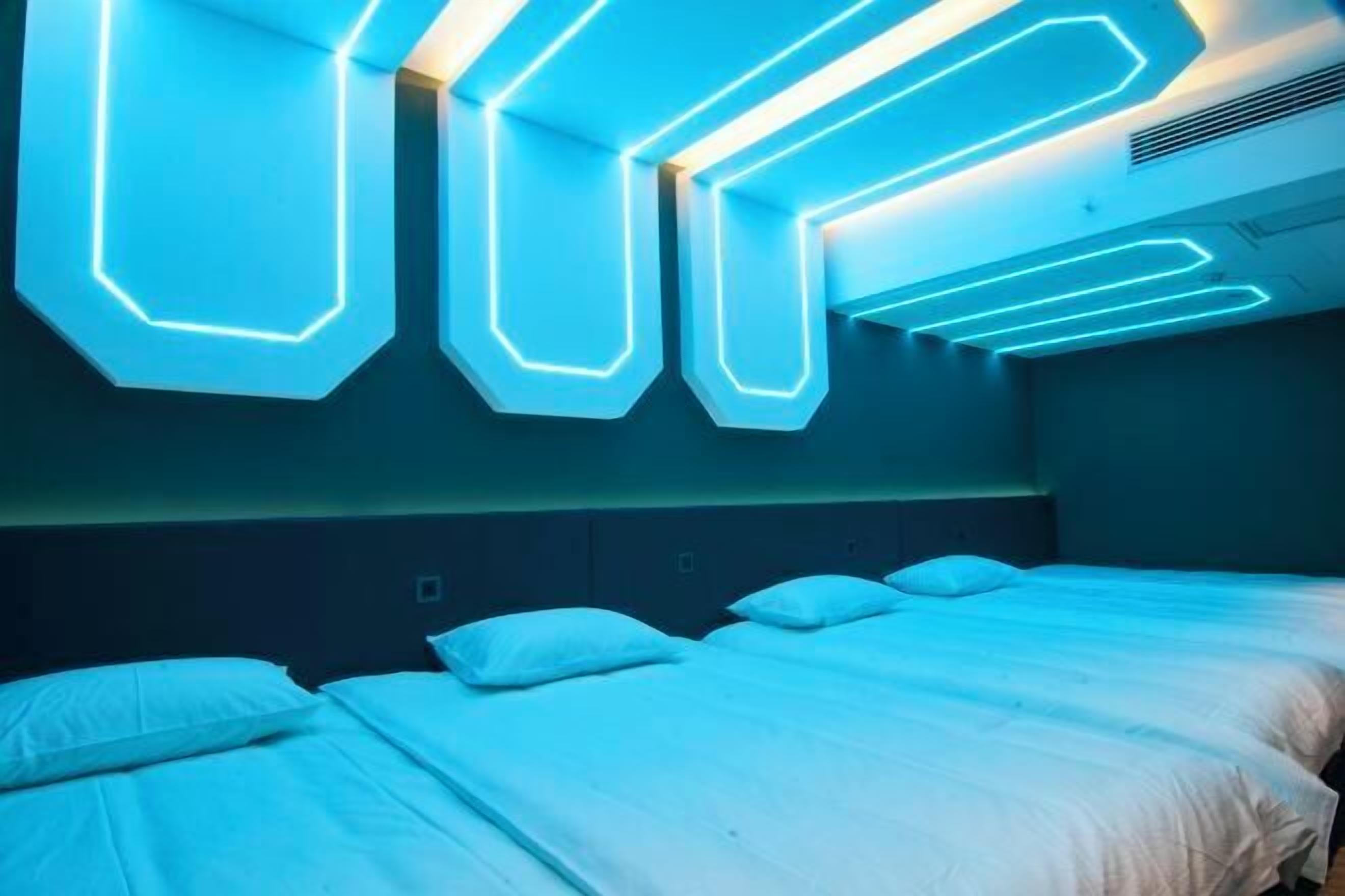 A hotel room with a modern design, featuring a bed with white bedding and a headboard with built-in lighting.