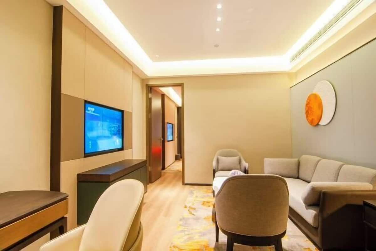 A hotel room with a TV, a sofa, a chair, and a desk.