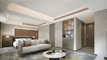 A modern hotel room with a sofa, a round coffee table, a bed, a nightstand, and a built-in kitchen area.
