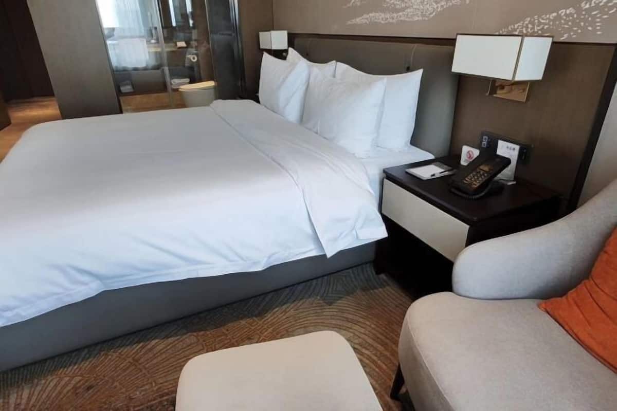 A hotel room with a large bed, a bedside table with a phone, and a chair.