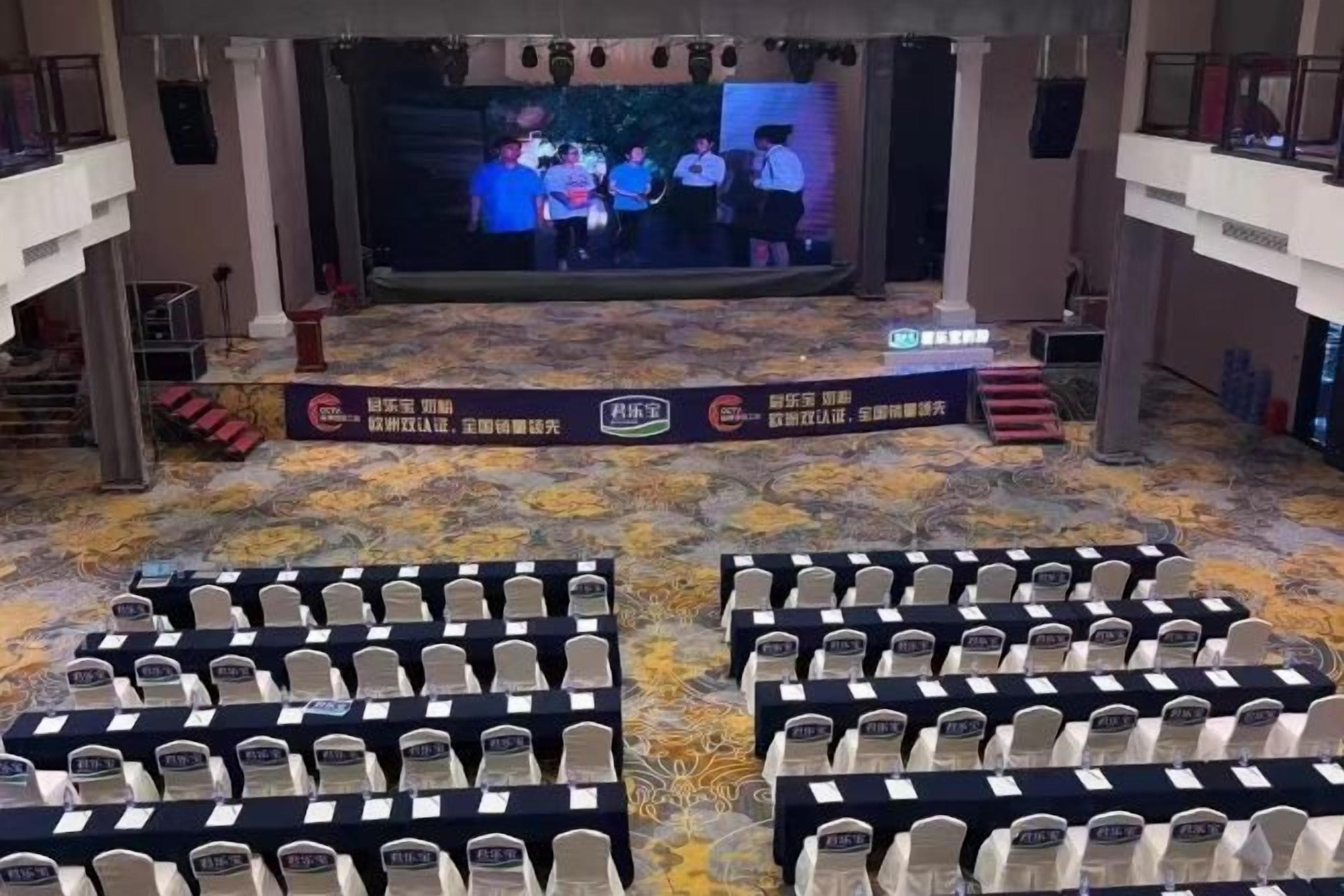A conference room with rows of chairs, a stage with a screen, and banners.