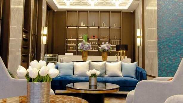 A modern lobby with a blue sofa, white chairs, a round table with a vase of flowers, and a decorative ceiling. - Huayuan Hotel (Xiantao)