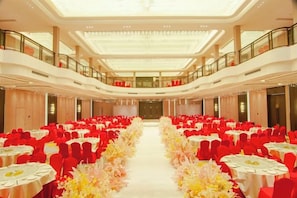 A large banquet hall with multiple tables arranged in rows, a central aisle, and a high ceiling with a glass panel. - Huayuan Hotel (Xiantao)