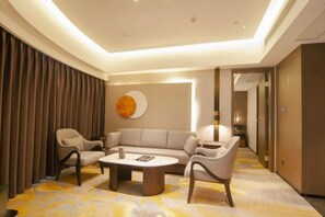 Moderni hotellihuone, jossa on sohva, kaksi nojatuolia, sohvapöytä ja suuri ikkuna.