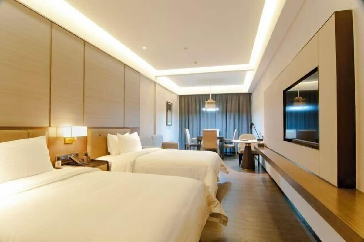 A hotel room with two beds, a desk, a chair, a TV, and a large mirror.
