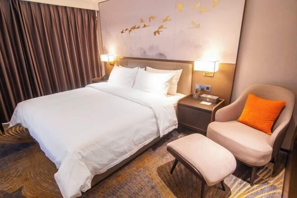 A hotel room with a large bed, a nightstand, a chair, and a wall with a bird mural.
