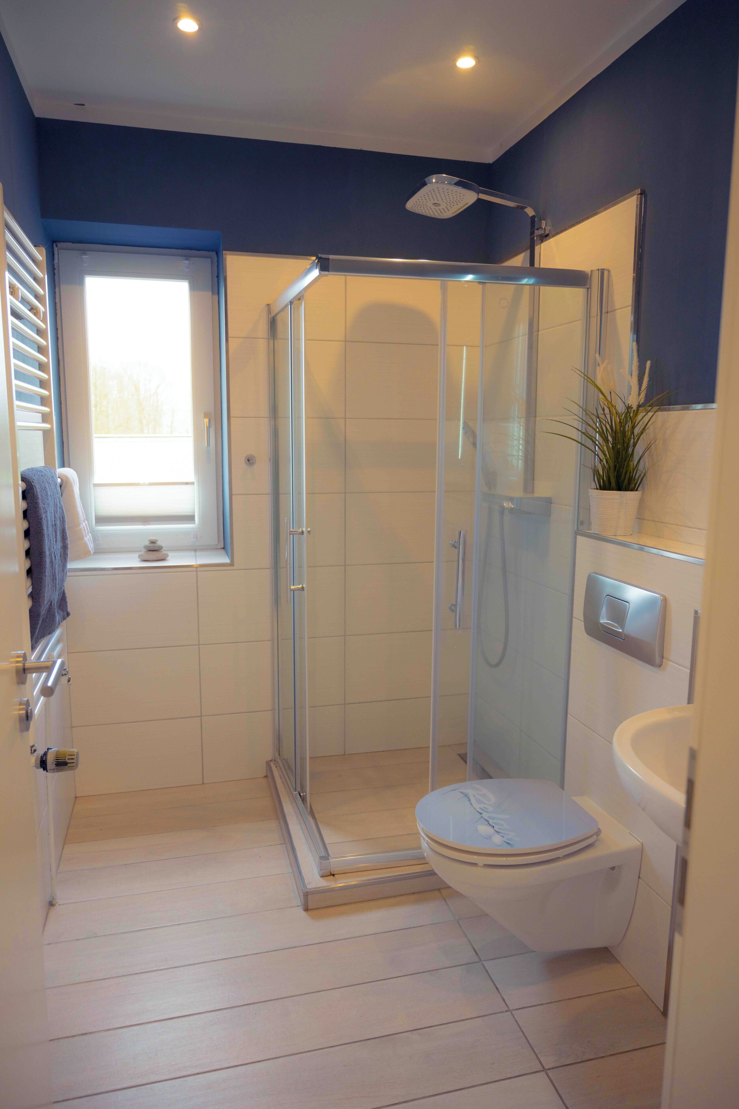 Un baño moderno con ducha envuelta en vidrio, inodoro, lavabo y ventana.