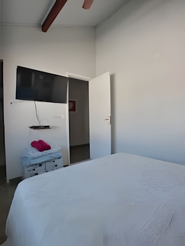 A bedroom with a bed, a television mounted on the wall, and a door leading to another room.