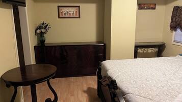 A bedroom with a bed, a dresser, a small table, and a wall-mounted shelf with a framed picture.