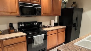 Una cocina con armarios de madera, estufa negra, microondas, refrigerador y encimera de granito.