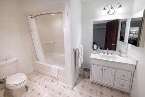 Une salle de bain avec des toilettes blanches, une baignoire, un lavabo et un meuble-lavabo avec des placards.