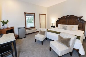 Une chambre d’hôtel avec un grand lit, deux fauteuils, un bureau et une petite table. Il y a une fenêtre donnant sur un paysage verdoyant.