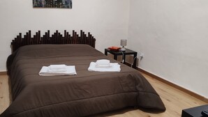 Een slaapkamer met een bed, een nachtkastje, een lamp, een schilderij van een stadsgezicht en een raam met gordijnen.