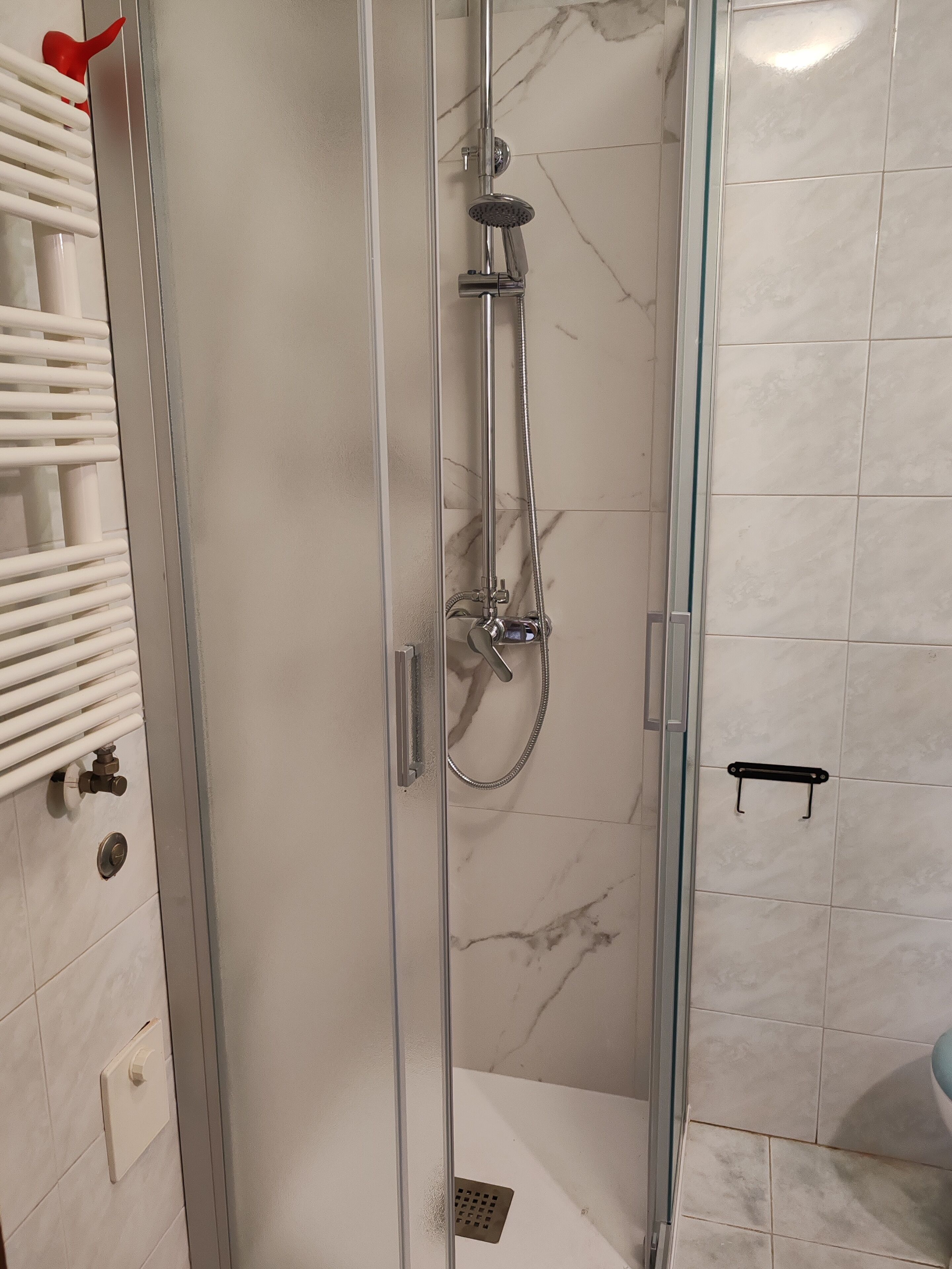 A glass-enclosed shower stall with a handheld showerhead and a handheld shower attachment.