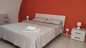 A neatly made bed with a patterned bedspread and pillows, a bedside table with a lamp, and a drawer unit.