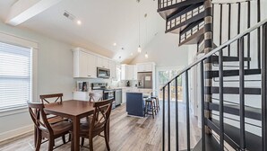 A modern kitchen with white cabinets, a central island, and a dining area with wooden chairs. - Outer Banks Cottage Gem! (Powells Point)