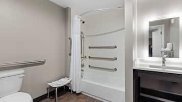 A bathroom with a white toilet, a shower with grab bars, a small step stool, and a mirror above the sink.