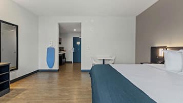 Una habitación de hotel con cama, escritorio, silla, espejo y puerta que da a un baño.