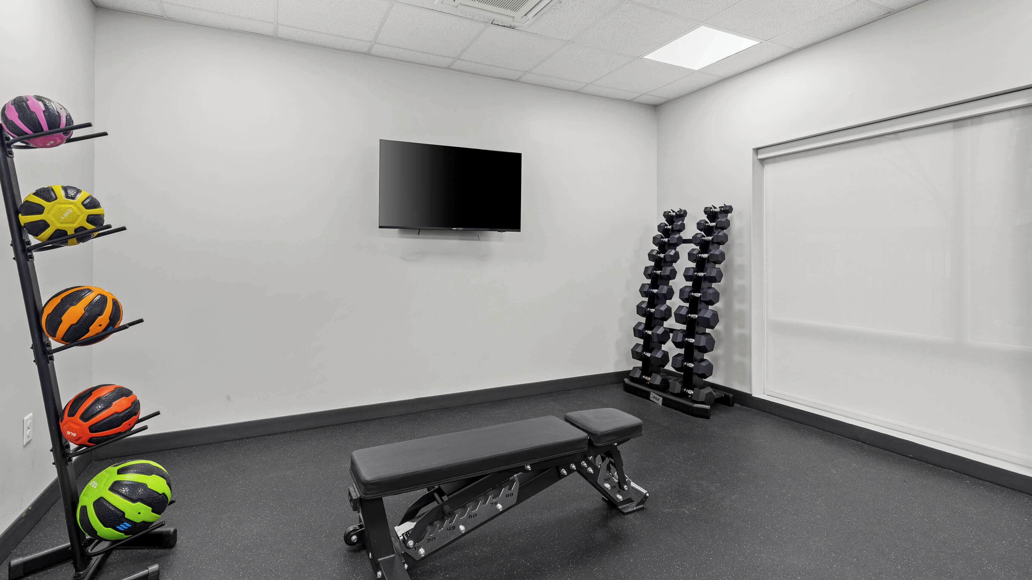 A gym with a bench, wall-mounted TV, and various exercise equipment.