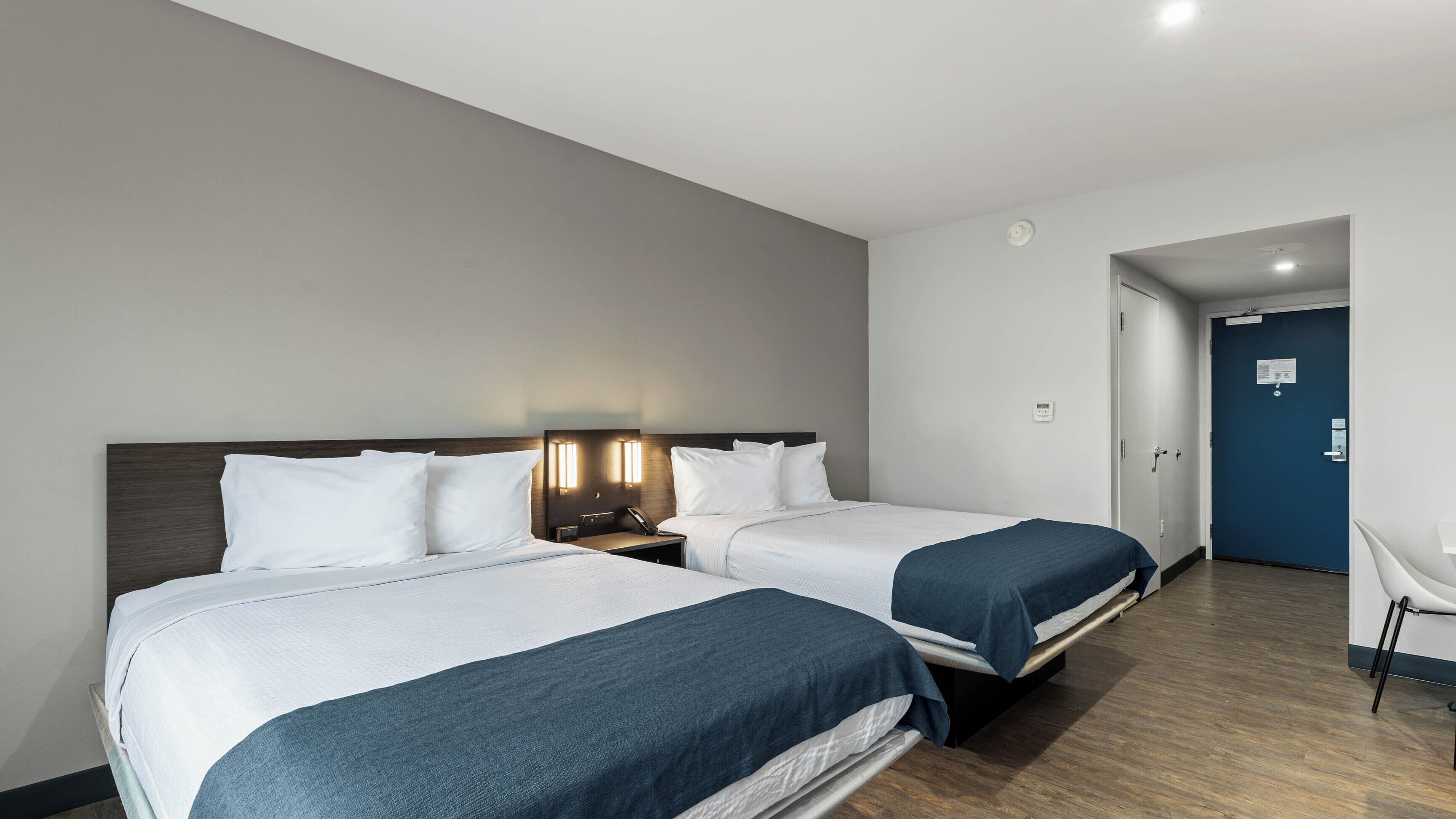 A hotel room with two beds, a desk, and a chair.