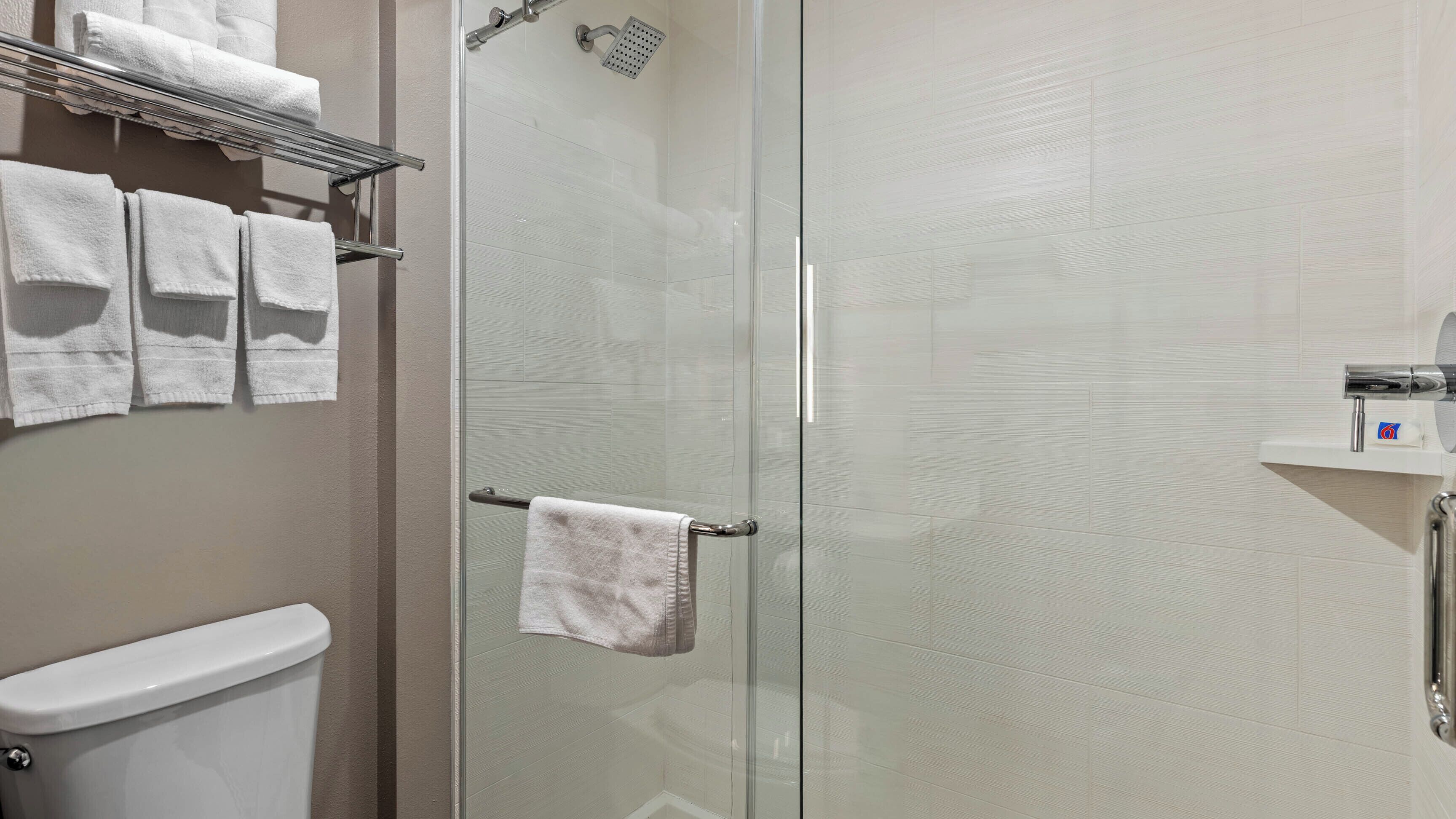 A bathroom with a glass shower door, a toilet, and a towel rack with multiple towels.