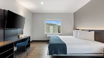 Una habitación de hotel moderna con cama, escritorio, silla, televisión y ventana con vista a edificios.