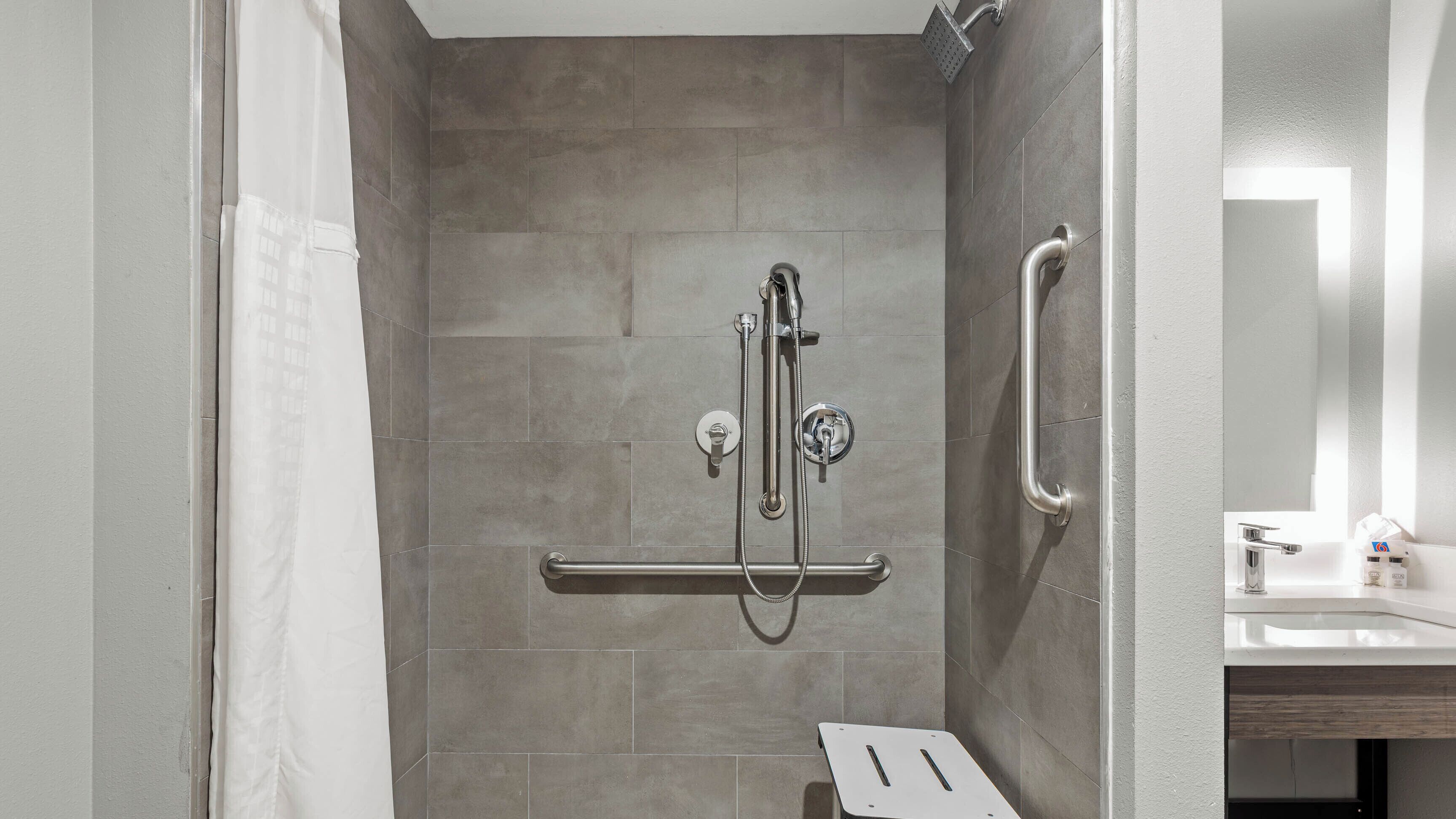 A shower with a handheld showerhead, a handheld showerhead, and a grab bar.
