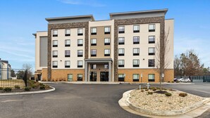 A multi-story hotel with a central entrance, parking lot, and landscaped area. - Studio 6 Richmond Airport (Sandston)