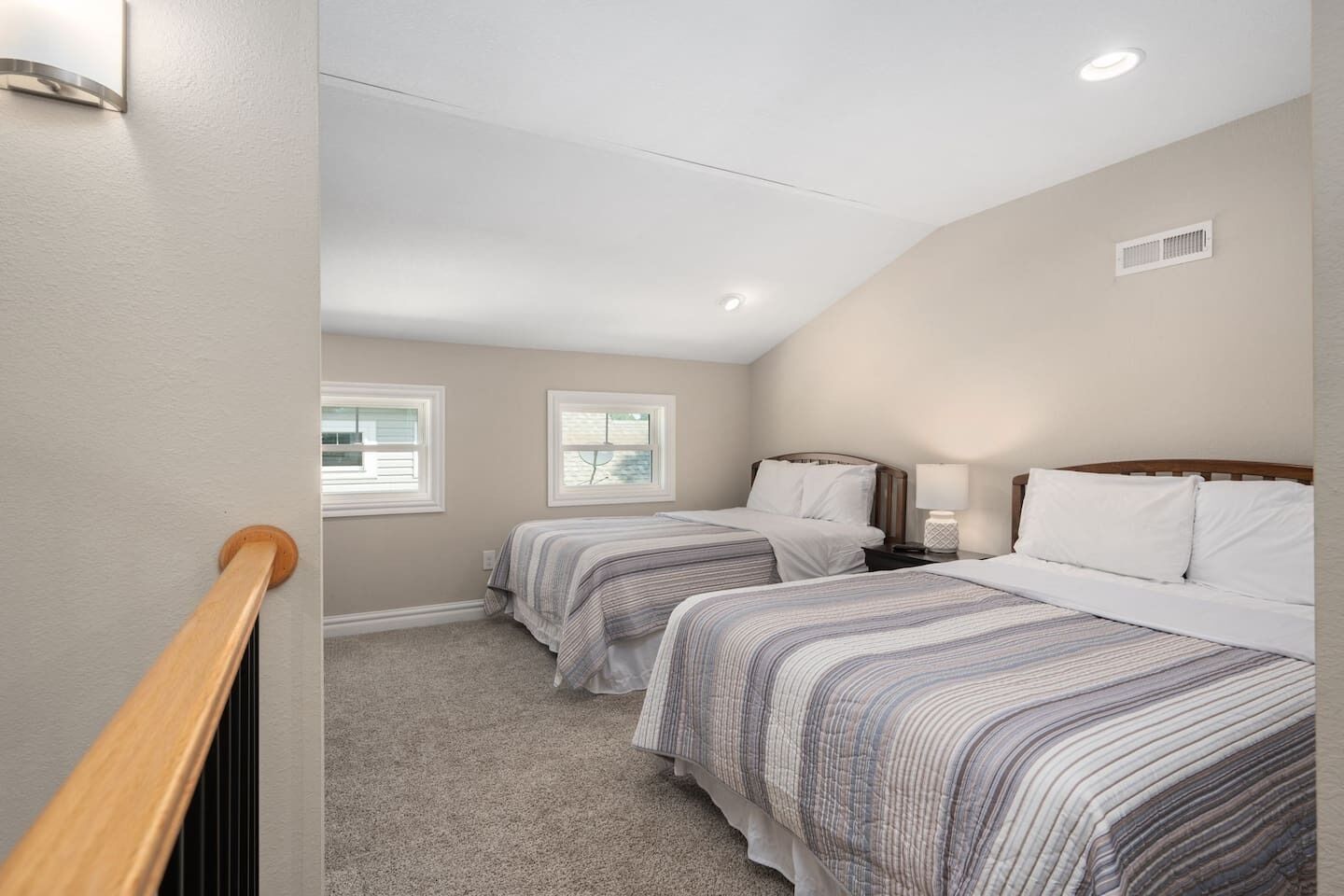 A bedroom with two beds, a wooden railing, and a sloped ceiling.