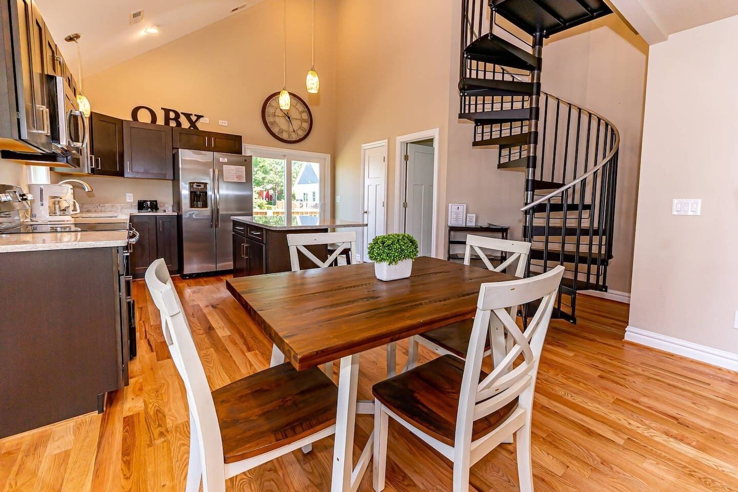 A modern kitchen with a wooden dining table, white chairs, and a spiral staircase.