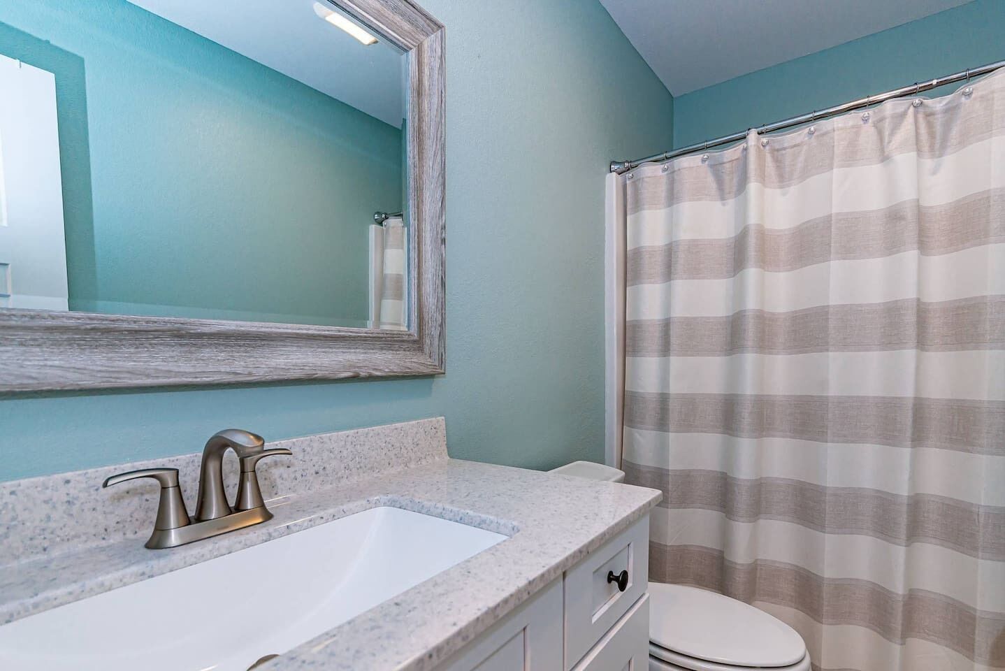 A bathroom with a white sink, a mirror, a shower curtain, and a toilet.