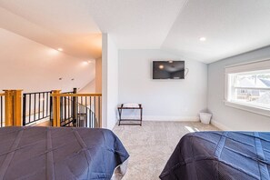 A bedroom with two beds, a TV on the wall, a window with a view, and a staircase.