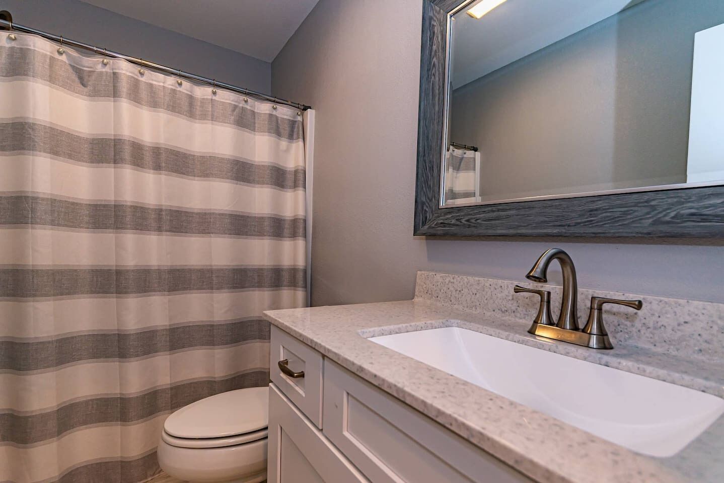 Une salle de bain avec un rideau de douche à rayures, un lavabo blanc avec un robinet doré et un miroir au-dessus du lavabo.