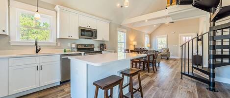 A spacious kitchen with a central island, white cabinetry, and a modern staircase.