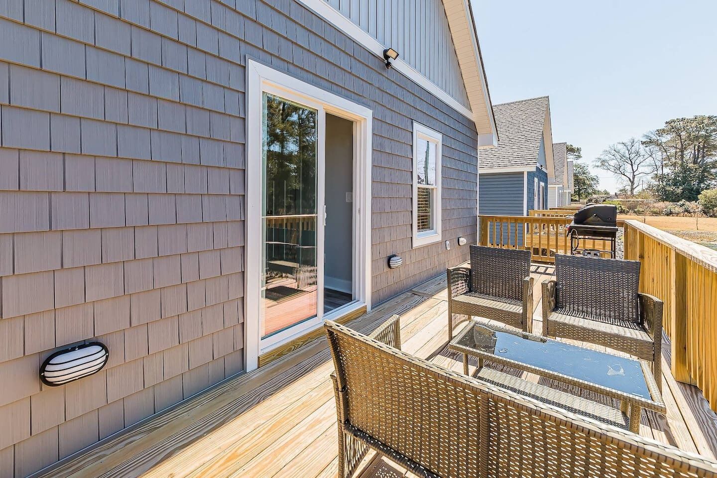 A deck with wicker furniture and a barbecue grill, adjacent to a house with a sliding glass door.