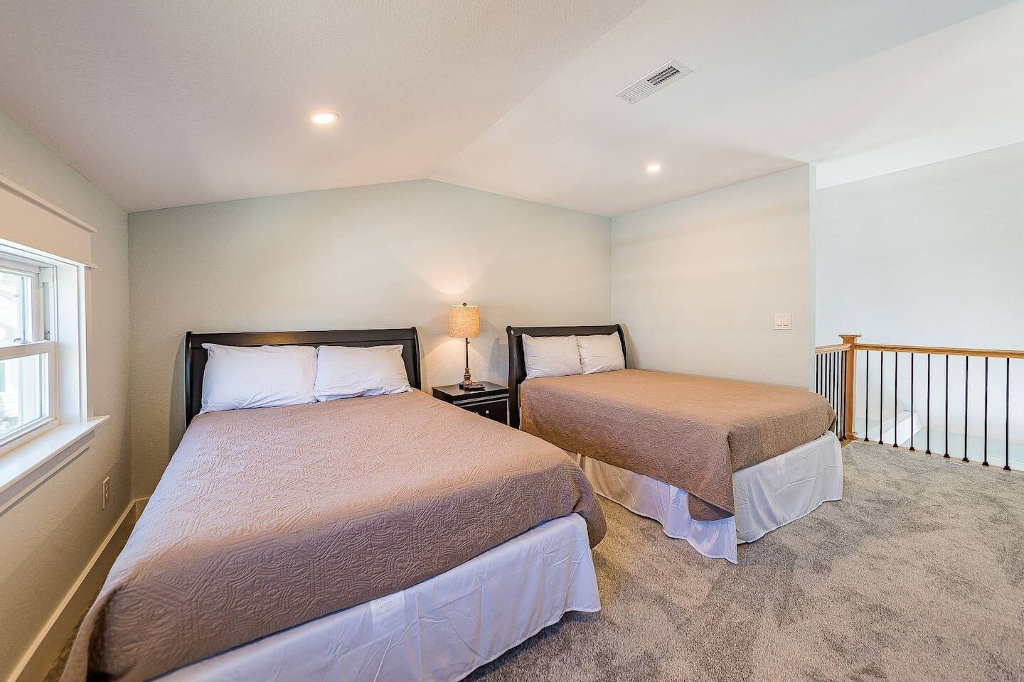 A bedroom with two beds, a window, and a nightstand with a lamp.