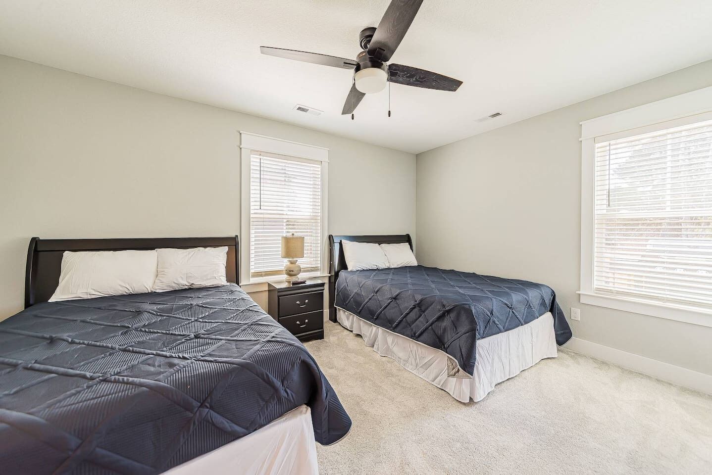 A bedroom with two beds, a ceiling fan, and a nightstand with a lamp.