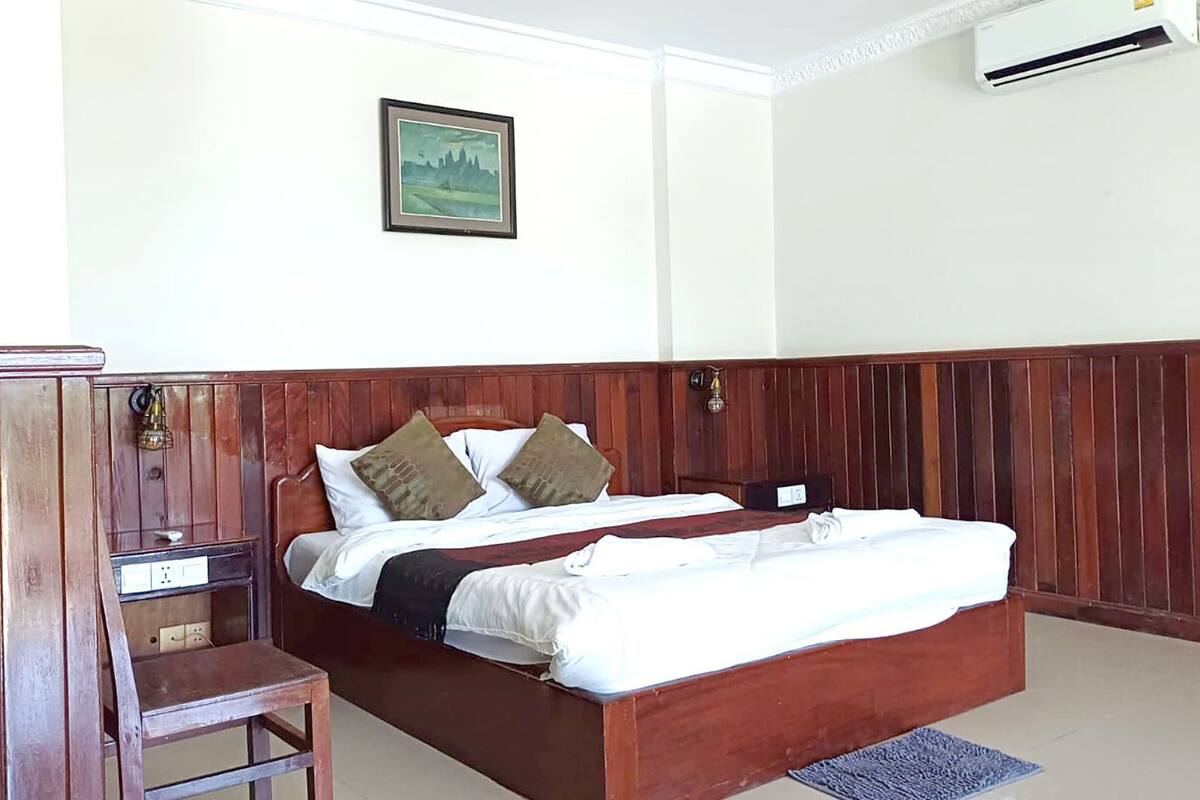 A bedroom with a wooden bed, a chair, a bedside table, and a wall-mounted air conditioner.