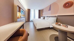 A hotel room with a bed, a desk, a chair, a small table, and a wall-mounted shelf.
