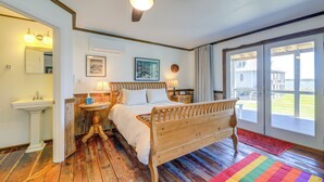 Une chambre avec un lit en bois, un ventilateur de plafond, une table de chevet avec une lampe, une commode et une vue sur l’extérieur grâce à une porte-fenêtre coulissante.