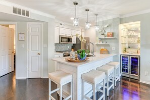 A modern kitchen with white cabinetry, a central island with bar stools, stainless steel appliances, and decorative plants. - Waterfront Lake Norman Retreat w/ Balcony (Davidson)