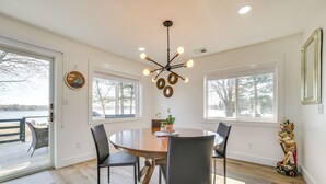 Uma sala de jantar com uma mesa redonda, quatro cadeiras, um candelabro e vista para o exterior.