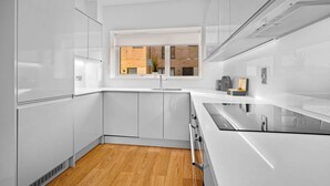 Een moderne keuken met witte kasten, een houten vloer en een raam met uitzicht op een gebouw van baksteen.