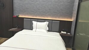 A hotel room with a large bed, a nightstand with a phone, and a wall-mounted light.