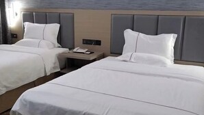 A hotel room with two beds, a nightstand, and a wall-mounted phone.